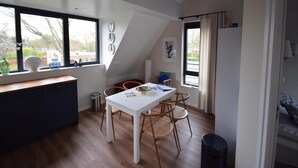 A modern kitchen with a white table, wooden chairs, and large windows. - Coastal Apartment in Oostkapelle (Oostkapelle)