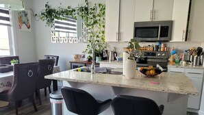 A modern kitchen with a central island, bar stools, a microwave, and various kitchen appliances. - Rapperswill Serenity (Edmonton)