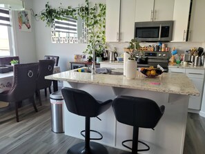 A modern kitchen with a central island, bar stools, a microwave, and various kitchen appliances. - Rapperswill Serenity (Edmonton)