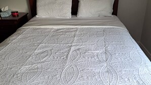 A neatly made bed with a patterned bedspread, a wooden headboard, and a bedside table with a tissue box and a red object. - Rapperswill Serenity (Edmonton)