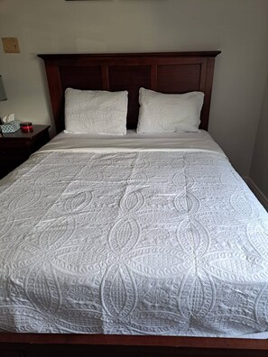 A neatly made bed with a patterned bedspread, a wooden headboard, and a bedside table with a tissue box and a red object. - Rapperswill Serenity (Edmonton)