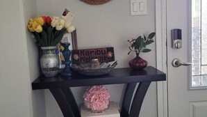 A home entryway with a black console table, a mirror, a welcome sign, a vase with flowers, a potted plant, and a door with a window. - Rapperswill Serenity (Edmonton)