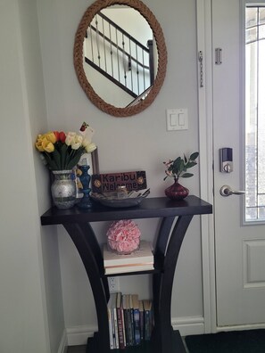 A home entryway with a black console table, a mirror, a welcome sign, a vase with flowers, a potted plant, and a door with a window. - Rapperswill Serenity (Edmonton)