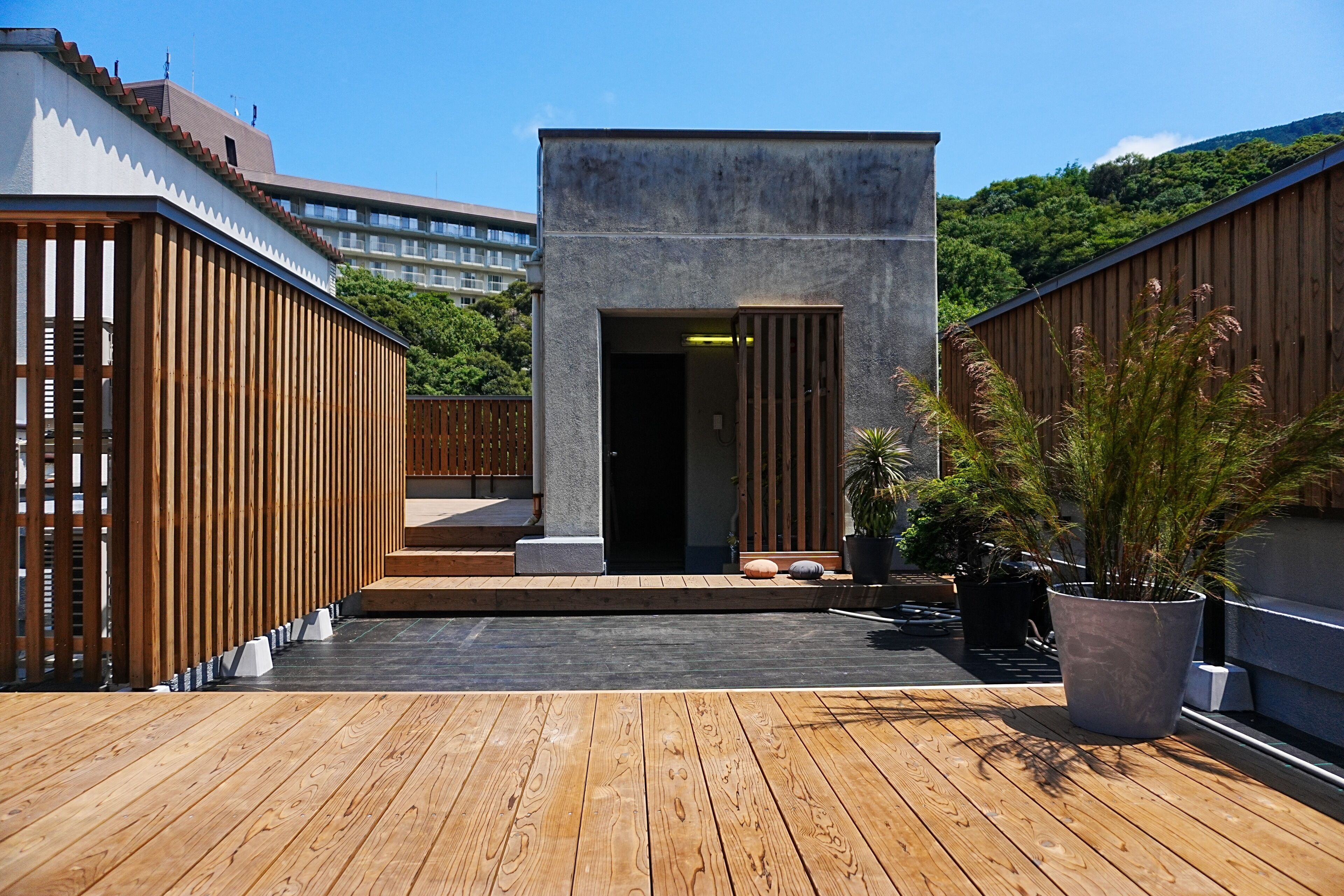 A rooftop terrace with a wooden deck, a concrete structure, and potted plants.