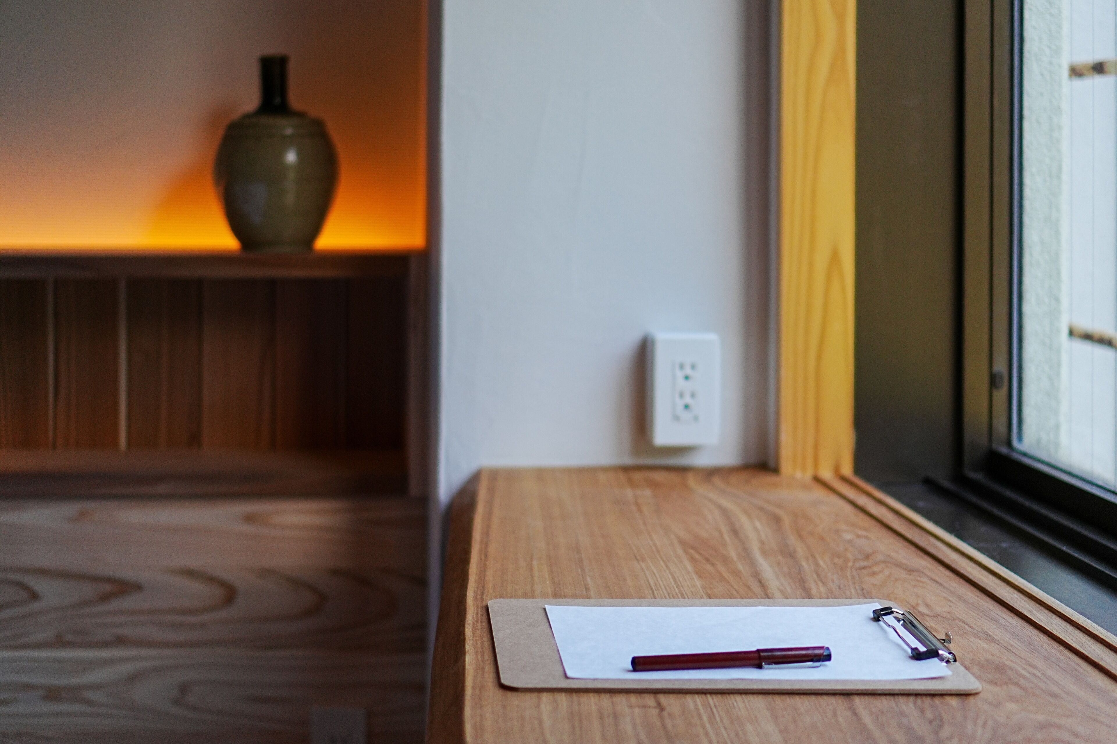 A wooden table with a clipboard, pen, and a vase in the background.
