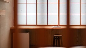 Una habitación con un escritorio de madera, un taburete y una ventana con diseño de cuadrícula.