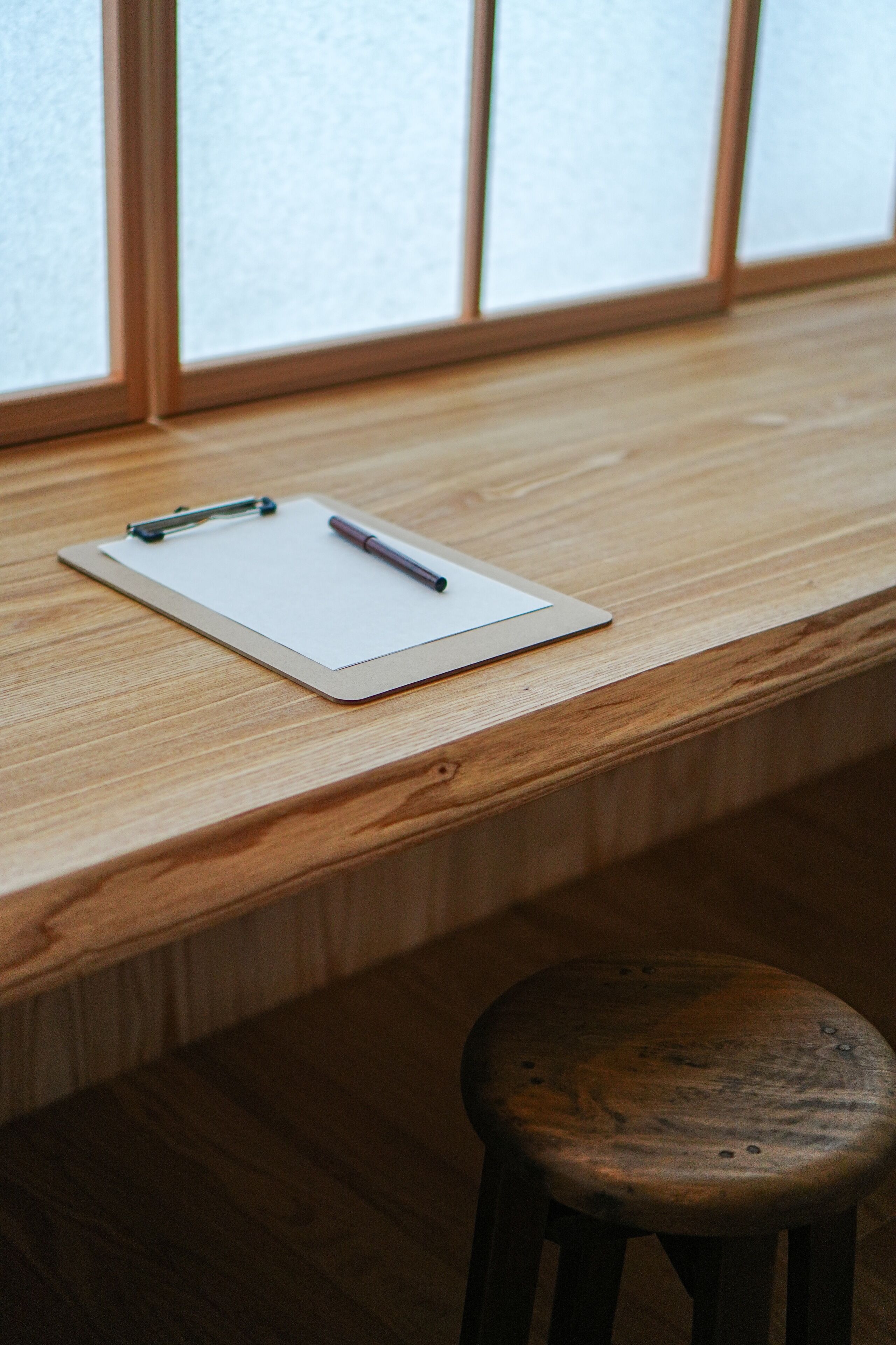 A wooden desk with a white notepad and pen, and a wooden stool.