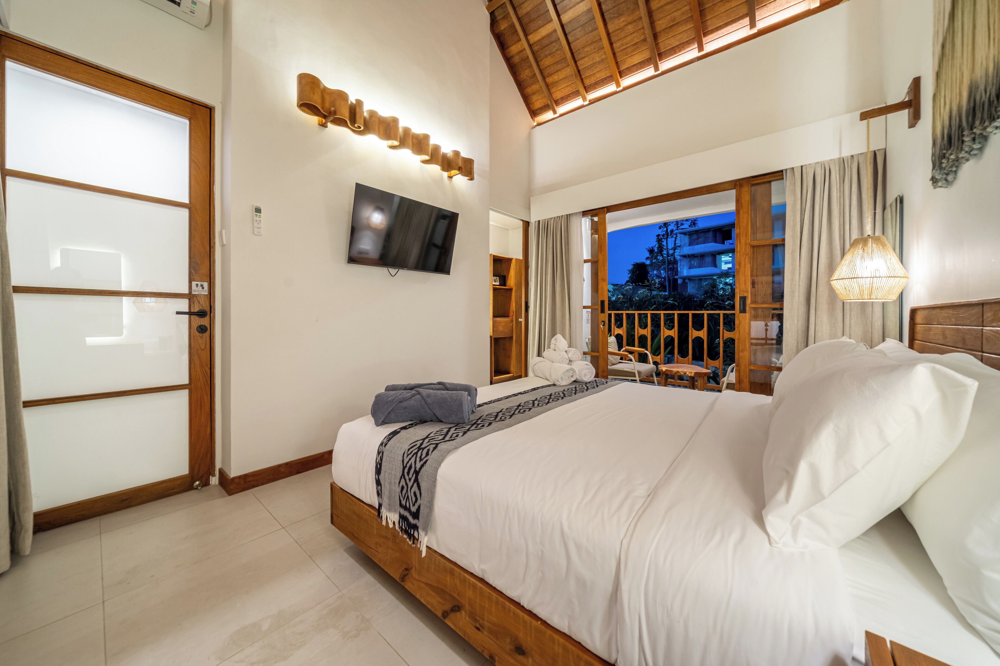 Ein Schlafzimmer mit einem großen Bett, einem Flachbildfernseher, einem Holz-Kopfteil und Blick ins Freie.