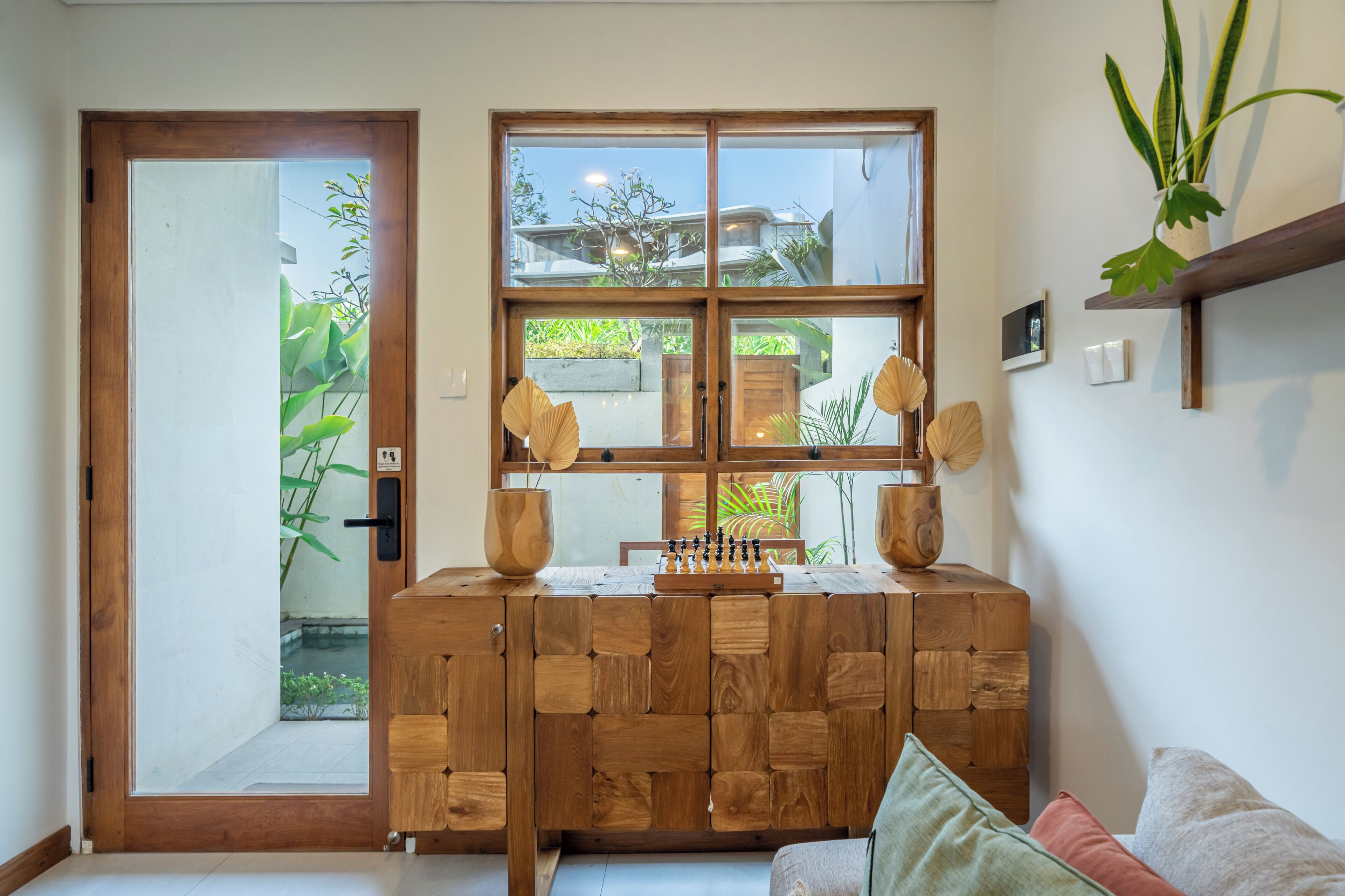Ein Holzkabinett mit einem Schachbrett, einer Tür und einem Fenster mit Blick auf Grünflächen.