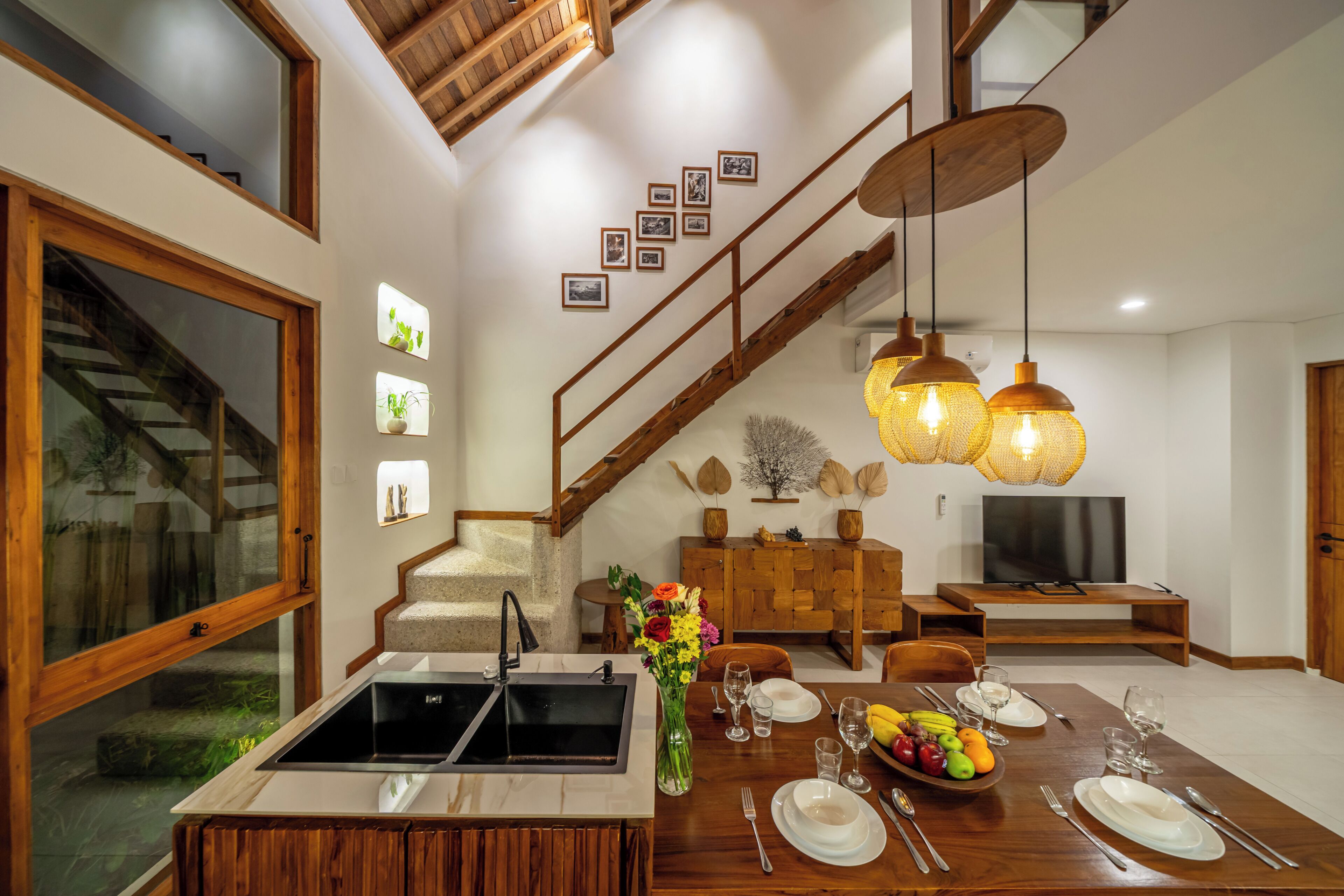 A modern kitchen with a sink, dining table set for four, and a staircase leading to an upper level.
