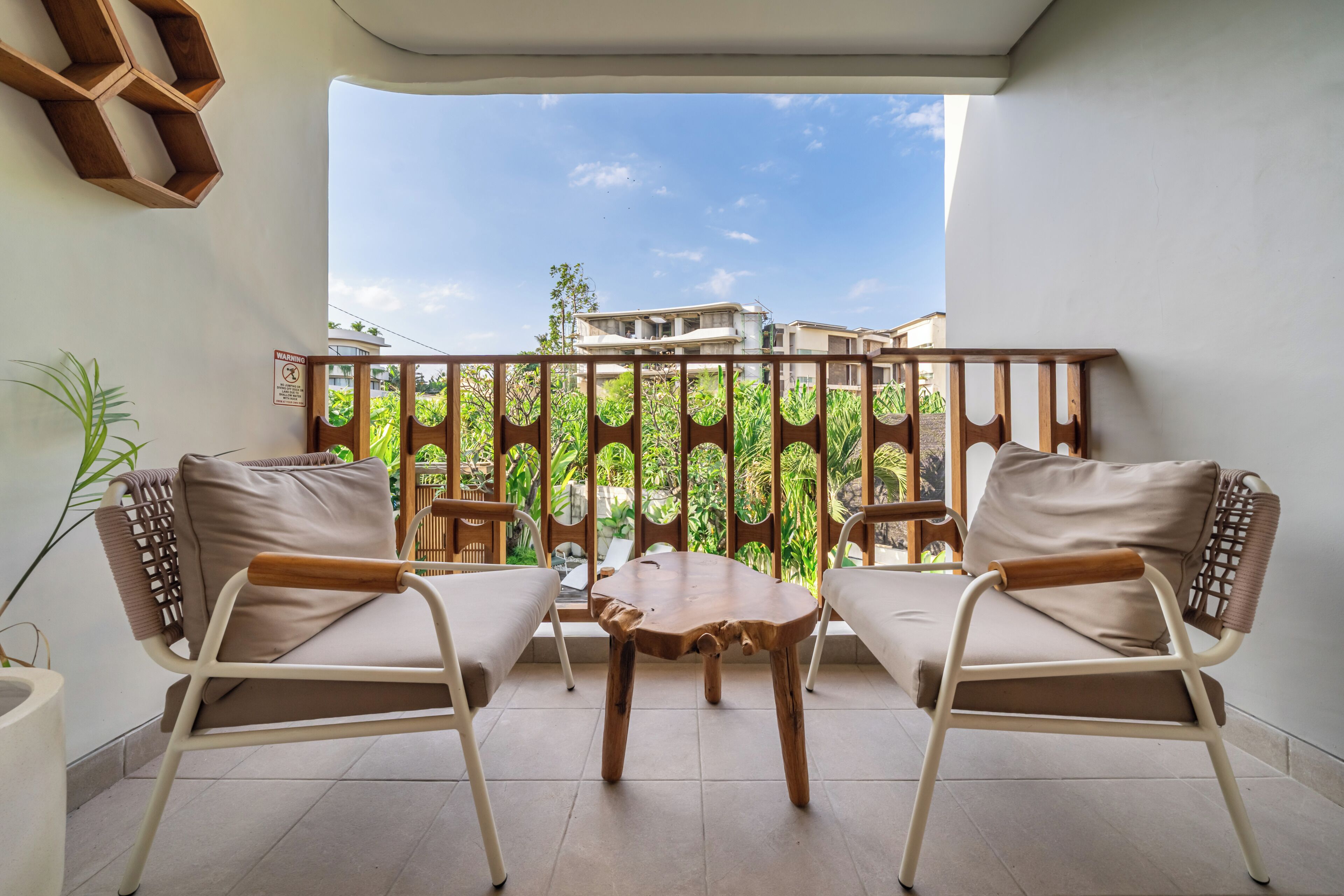 A balcony with two chairs and a table, a wooden partition, and a view of buildings and greenery.