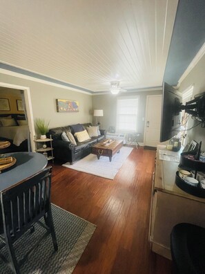 A living room with a sofa, coffee table, and a dining area with chairs and a table. - Peaceful River View Condo (Townsend)