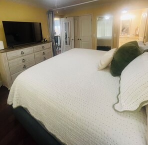 A bedroom with a bed, a television on a dresser, a door, and a mirror. - Peaceful River View Condo (Townsend)