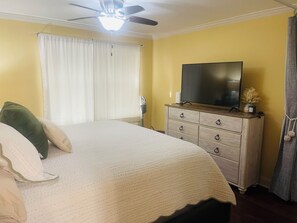 A bedroom with a bed, a dresser, a television, and a ceiling fan. - Peaceful River View Condo (Townsend)