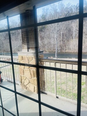 A stone fireplace with a metal railing in front of a window overlooking a grassy area and trees. - Peaceful River View Condo (Townsend)