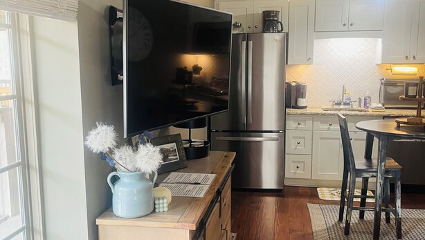 Una cocina moderna con televisor de pantalla plana, electrodomésticos de acero inoxidable y un comedor con mesa y sillas de madera.
