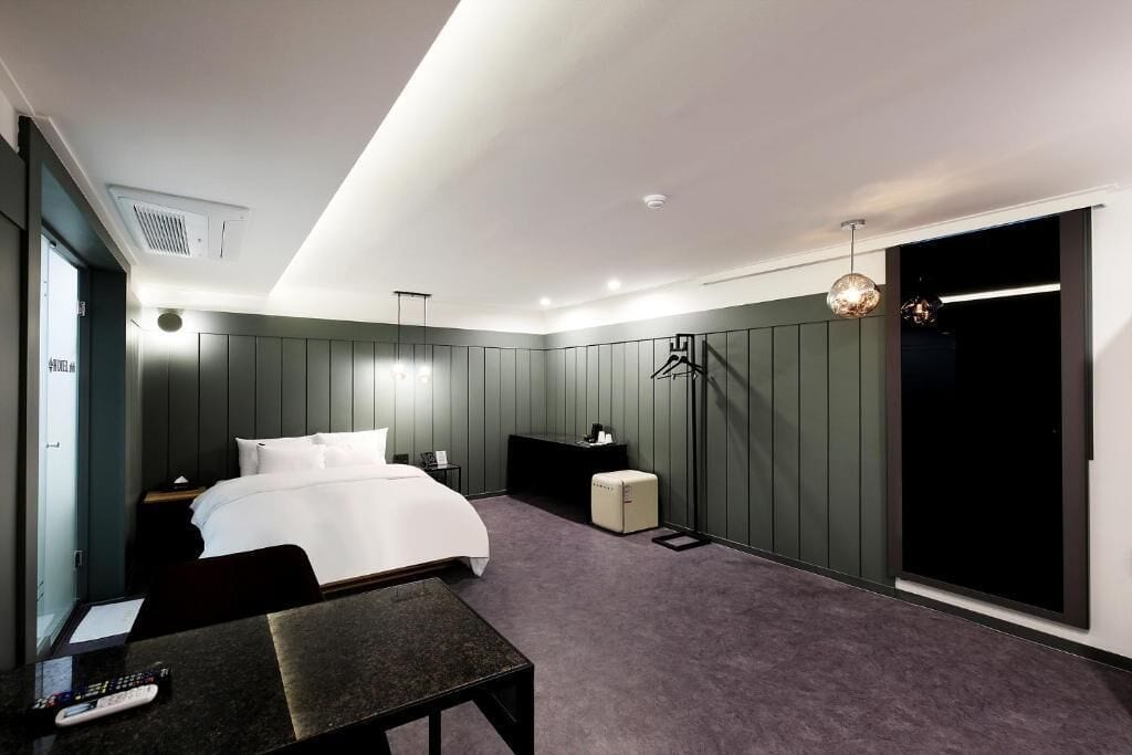 A modern hotel room with a bed, bedside table, and a desk with a chair.