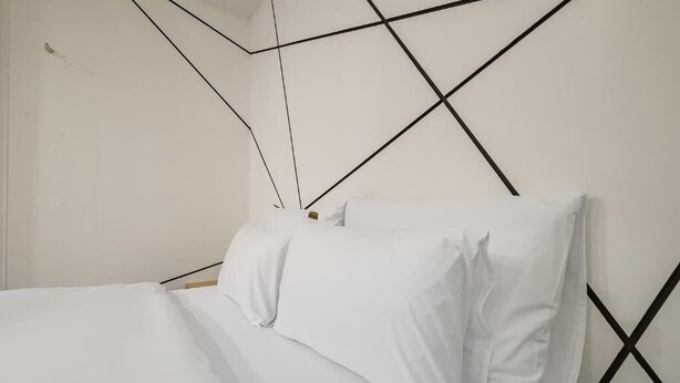 Una cama con ropa de cama y almohadas blancas, cabecera de madera y diseño geométrico en una pared negra.