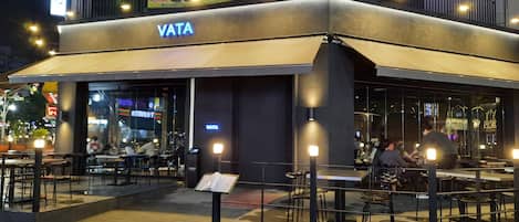 An outdoor seating area of a restaurant with tables and chairs, a sign for 'VATA', and a phone number '233-3853' above the entrance.