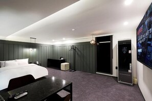 Quarto de hotel com cama, escrivaninha, cadeira, televisão, guarda-roupa e porta de acesso a um banheiro.