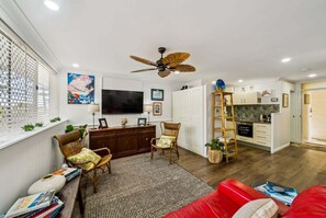 A living room with a TV, wooden furniture, a red sofa, and a kitchen area. - Beachfront Burleigh Getaway! (Gold Coast)