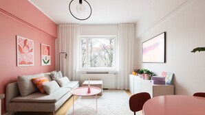 Een moderne woonkamer met een bank, een klein rond tafeltje, een radiator en een raam met uitzicht op gebouwen.