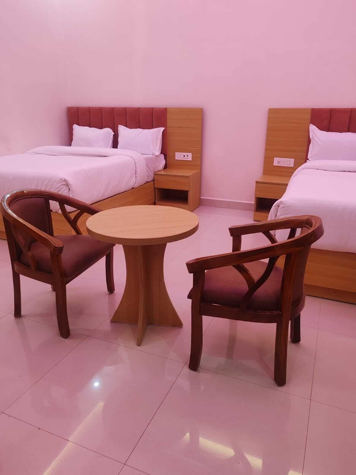 A hotel room with two beds, a round table, and two wooden chairs.