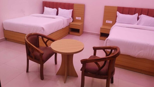 Una camera d'albergo con due letti, un tavolo rotondo in legno e due sedie di legno.