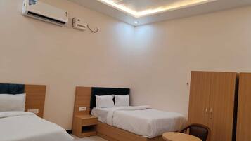 Habitación de hotel con dos camas, ventilador de techo, unidad de aire acondicionado, una mesita y un armario.