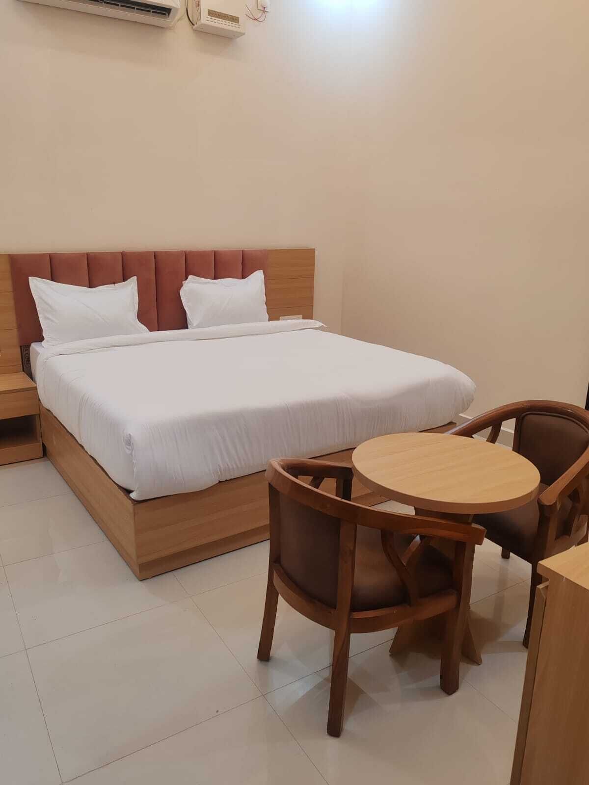 Une chambre d’hôtel comprenant un lit, des tables de chevet, une table ronde en bois avec des chaises et un climatiseur fixé au mur.