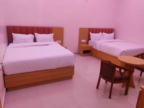 A hotel room with two beds, a wooden nightstand, a wooden chair, and a small round table. - Laxmi Seva Sadan Laxmi Hotel  (Barsana)