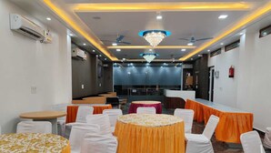 A conference room with round tables, white chairs, and orange tablecloths. - Laxmi Seva Sadan Laxmi Hotel  (Barsana)