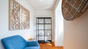 Een kamer met een blauwe bank, een zwarte boekenkast met decoratieve objecten, en een wandkleed.