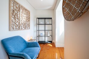 A room with a blue sofa, a black shelving unit with decorative items, and a woven wall hanging. - GuestReady - Charming Apartment in Lisbon 3E (Lisbon)