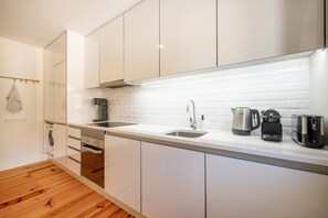 A modern kitchen with white cabinets, a stainless steel sink, a coffee maker, and a kettle. - GuestReady - Charming Apartment in Lisbon 3E (Lisbon)