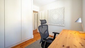 Een moderne kamer met een houten bureau, een zwarte bureaustoel, een witte garderobe en een decoratief wandpaneel.