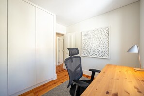 A modern room with a wooden desk, a black office chair, a white wardrobe, and a decorative wall panel. - GuestReady - Charming Apartment in Lisbon 3E (Lisbon)