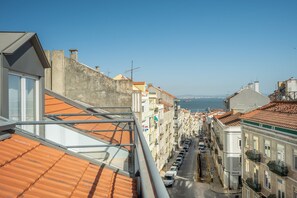 A narrow street with buildings on both sides, a clear view of the sea, and parked cars. - GuestReady - Charming Apartment in Lisbon 3E (Lisbon)