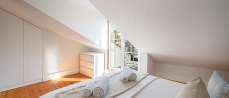 Un dormitorio con tragaluz, una cama con toallas enrolladas, una mesita de noche y vistas de la ciudad a través de la ventana.