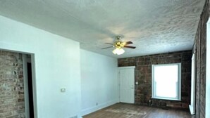 Ein Zimmer mit Deckenventilator, Backsteinwand, Holzboden und Fenster.