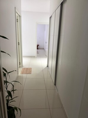 A hallway with white walls, a wooden mat, and a plant. - Holiday Homes - Newtown Apartment 1 (Nadi)