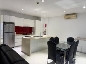 A modern kitchen with a central island, stainless steel appliances, and a dining area with a glass table and black chairs. - Holiday Homes - Newtown Apartment 1 (Nadi)