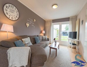 A living room with a sofa, a coffee table, a TV, a clock, and a wall with heart-shaped decorations. - Holiday Home With Private Parking (Oostkapelle)