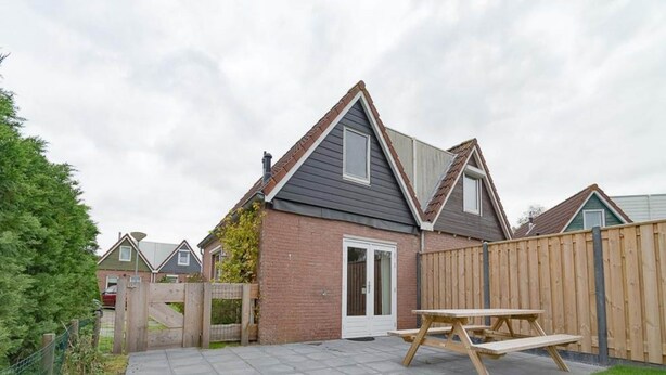 A residential backyard with a paved patio, a wooden fence, and a house with a grey roof and brick walls. - Holiday Home With Private Parking (Oostkapelle)