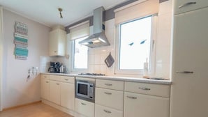A kitchen with white cabinets, a microwave, a stove, and a window with blinds. - Holiday Home With Private Parking (Oostkapelle)
