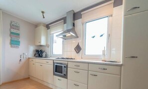 A kitchen with white cabinets, a microwave, a stove, and a window with blinds. - Holiday Home With Private Parking (Oostkapelle)