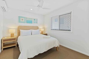 A bedroom with a bed, two bedside tables, a ceiling fan, a window with blinds, and wall art. - 8 / 39 Albatross Avenue (Gold Coast)