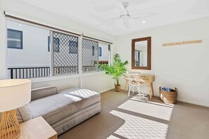 Un salon moderne avec un canapé, une petite table, une plante en pot, un miroir et un ventilateur de plafond.