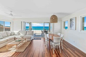 A spacious living area with a large window overlooking the ocean, a ceiling fan, a dining table with chairs, and a woven pendant light. - 8 / 39 Albatross Avenue (Gold Coast)