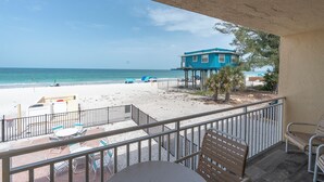 Un balcón con vista a la playa, un edificio azul y una mesa con sillas.